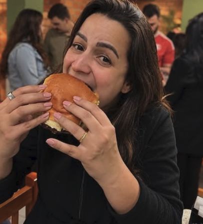 Cliente sorrindo enquanto morde um lanche no salão cheio
